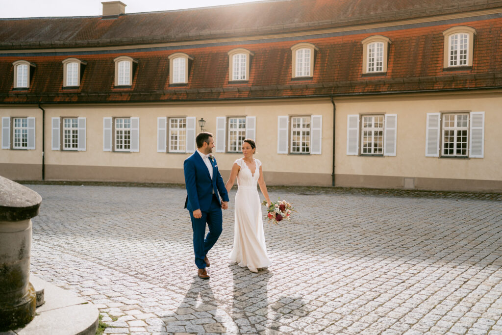 Hochzeitsfotograf Stuttgart: Brautpaar läuft Hand in Hand an Schloss Solitude entlang