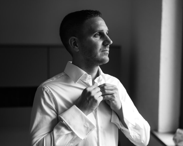 Bräutigam beim Getting Ready wie er sein Hemd zuknüpft