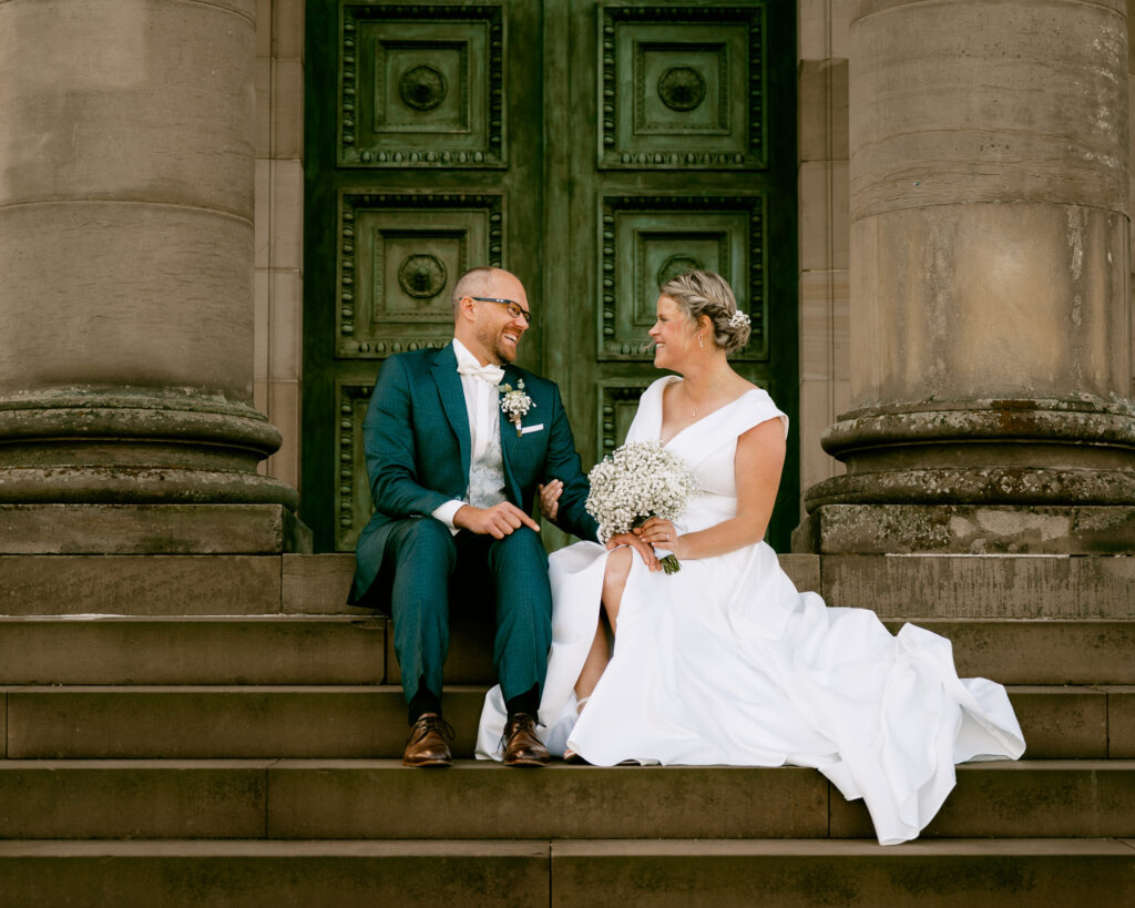 Hochzeitsfotograf Grapkapelle Stuttgart: Brautpaar sitzt auf den Treppen der Grabkapelle und lacht ausgelassen.